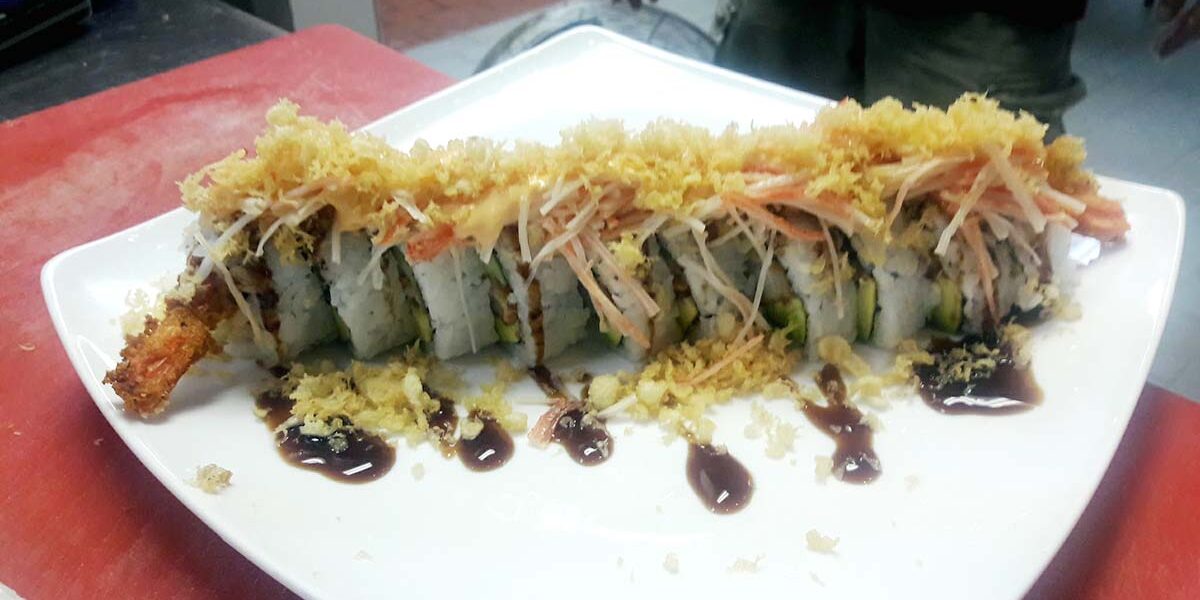 A sushi roll with sauce and rice on top.