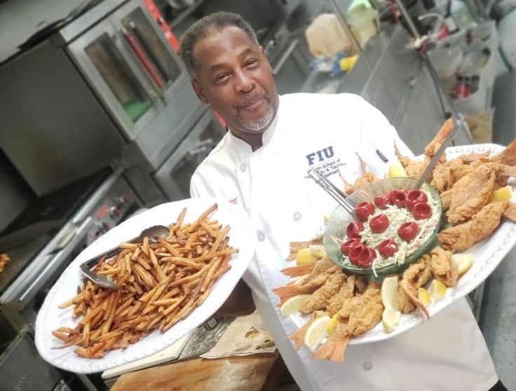 A man in chef 's outfit holding plates of food.